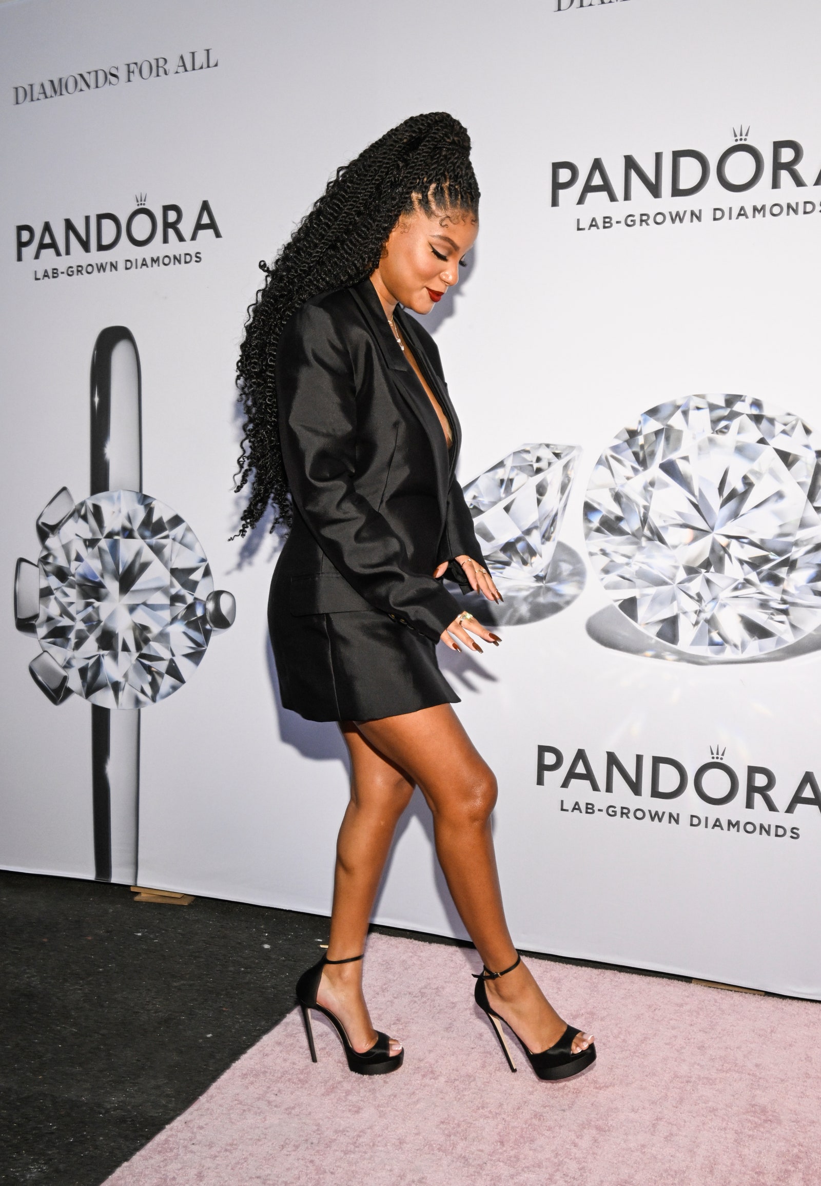 Halle Bailey appears at an event in a black blazer dress. She wears her hair in a high ponytail.